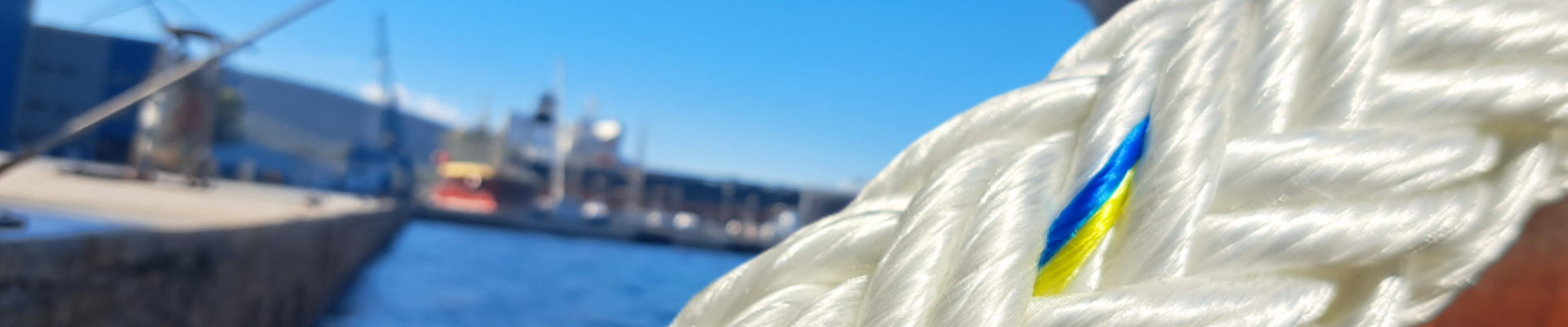 Close-up of UV-resistant synthetic mooring rope by Katradis, dockside with vessels in the background under clear blue sky