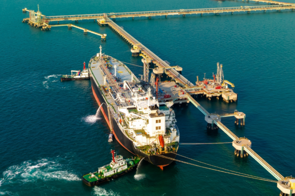 Oil tanker moored at offshore terminal with tugboat assistance and mooring lines connected to jetty
