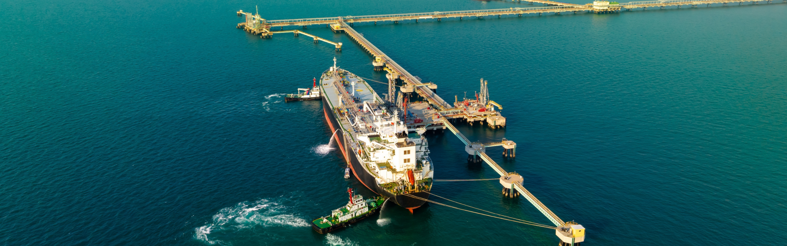 Oil tanker moored at offshore terminal with tugboat assistance and mooring lines connected to jetty